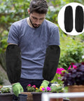 Tough As Nails Four Pack Waterproof Arm Sleeves With Thick Elbow Guards Grease Proof Oil Resistant Protective Oversleeves For Mechanics Shop Floor And Weekend Grind In Black worn by a man while gardening.