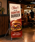 Heavy Duty Adjustable X Banner Stand With Sturdy Aluminum Frame and Durable Travel Case Perfect For Trade Shows Street Fairs Or Urban Hustles displaying a burger menu in a restaurant.