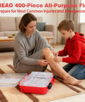 First aid kit, 400-piece, red plastic case, open on floor; woman bandages knee while child helps.