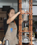Generous Eighty Four Oz Cold Brew Drip Tower Iced Coffee Maker with hand blown glass vessel, wooden base, brewing process shown.