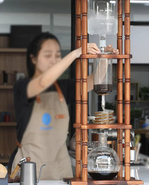 Generous Eighty Four Oz Cold Brew Drip Tower Iced Coffee Maker with hand blown glass vessel, wooden base, brewing process shown.