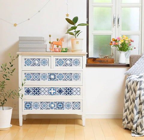 White dresser with decorative blue tile patterns in bright room, beside a window with plants and flowers.