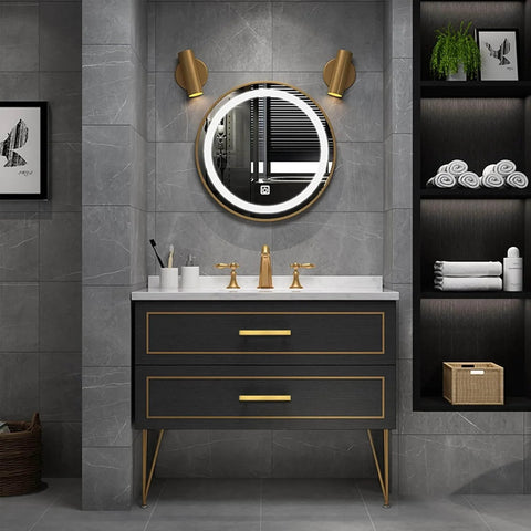 Modern bathroom with black vanity featuring gold cabinet pulls, round mirror, gold faucets, and grey tile walls.
