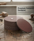 Grab This Heavy Duty Aluminum Oxide Sandpaper For Waterproof Projects Plus Coarse Grit Options in a stack on a wooden surface.