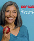 Smiling woman holding apple with text 'Hold That Makes Your Gums Happy' promotes All Day Hold Denture Adhesive Seals for Uppers in Fresh Mint.