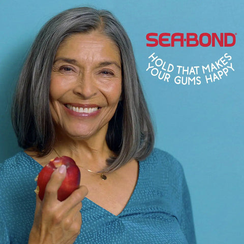 Woman smiling holding an apple, wearing Secure Denture Adhesive Seals For Upper Dentures Zinc Free All Day Hold No Mess Comfort Cushioned Release