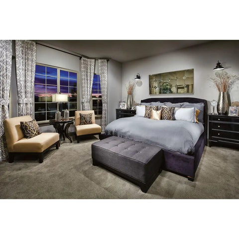 Elegant modern bedroom with plush gray bed, beige chairs, side tables, and patterned curtains overlooking a large window.