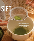 Hand holding a sifter over a bowl filled with green powder, used for Electric Matcha Whisk And Milk Frother With One Button Operation