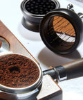 Pro Level 58mm Coffee Powder Distributor And Espresso Stirrer Tool Featuring Adjustable Height Dial Built From Food Grade Metal For Smooth Barista Extraction Plus Even Ground Bedding In Dope Gloss Black with coffee grounds in portafilter.
