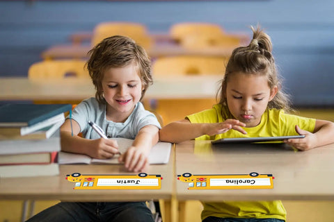 Children with School Bus Themed Desk Name Tags Set With 36 Self Adhesive Name Plates For Classrooms on desks in a classroom.