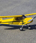 Yellow J-3 Cub Balsa Wood Model Airplane Kit With 46 Inch Wingspan on pavement, featuring realistic cowl and landing gear.