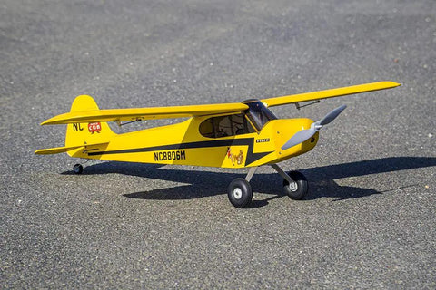 Yellow J-3 Cub Balsa Wood Model Airplane Kit With 46 Inch Wingspan on pavement, featuring realistic cowl and landing gear.