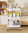 Three-Tier Folding Rolling Utility Cart With Wheels Foldable Storage Organizer With Three Hanging Cups And Six Hooks For Kitchen Office Living Room Nursery White Ideal For Home Organization And On The Go Use, placed in a nursery setting with toys and baby supplies.