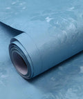 Roll of blue damask peel and stick wallpaper showing floral texture, suitable for easy DIY accent walls, vintage style.
