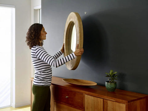 Person hanging a mirror using Claw Drywall Picture Hanger Set, Holds 45 Lbs Per Hook, Includes 3 Hooks And 3 Spot Markers, Stainless Steel Silver Finish, No Studs Needed, Heavy Duty Wall Hanging For Pictures And Mirrors on a black wall above a wooden console.