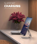 Adjustable Tablet Stand For 4 To 13 Inch Tablets And Phones Desktop Holder For iPad Pro Models Air Mini Kindle Switch Galaxy Tab And More Ideal Office Desk Accessory For Home And Work showcasing a charging tablet on a desk.