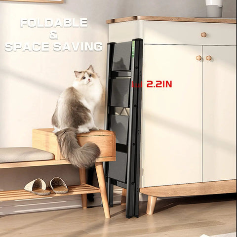 3 Step Folding Aluminum Ladder With Wide Anti Slip Pedals Portable Lightweight Step Stool For Home And Office Use Kitchen 330 Lb Capacity Black With Non Slip Rubber Feet For Extra Stability folded against kitchen cabinet next to a cat on a wooden stool.