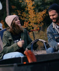 Two people enjoying a campfire beside an RV in a wooded area.