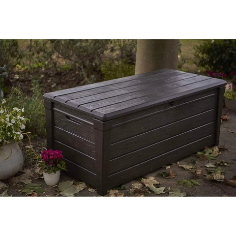 Lockable 120 Gallon Outdoor Storage Deck Box for Patio Backyard and Garden in Brown Waterproof Plastic Bench among plants.