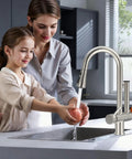 Premium Brushed Nickel Pull Down Kitchen Faucet With Built In Water Filter and Activated Carbon Ultrafiltration Spray Head Yields Crystal Pure Drinking Water in use by a mother and daughter.