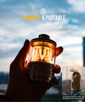 Hand holding Vintage Aluminum Camping Lantern With Dimmable 2100K Warm Glow, USB-C power, against sky backdrop