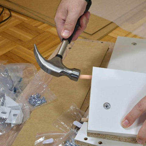 Person assembling furniture using 1000 Piece Five Sixteenth Inch Wooden Dowel Pins Set For Woodworking, with hammer and wood panels.