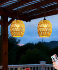 2 Pack Battery Operated Handwoven Natural Rattan Chandeliers Egg Shaped Boho Pendant Lights illuminated at dusk on a patio.