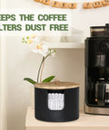 Wooden coffee filter holder and countertop storage jar with lid, next to a coffee machine, for easy organization.
