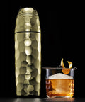 Vibes On Point 25 Oz Gold Vacuum Insulated Cocktail Shaker With Jigger And Strainer Featuring Dr Dre Snoop Dogg Collab next to an elegant cocktail.