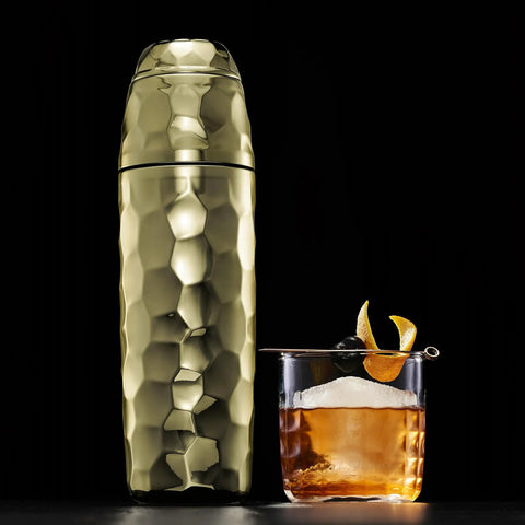 Vibes On Point 25 Oz Gold Vacuum Insulated Cocktail Shaker With Jigger And Strainer Featuring Dr Dre Snoop Dogg Collab next to an elegant cocktail.