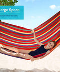 Child relaxing in a colorful Durable 320G Canvas Camping Hammock With 550Lbs Capacity on a beach.