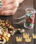 Crafting tools with Dope Vintage Style Crown Charms Set, 50 Pcs Alloy Gold Tone Crown Pendants, beads, and bracelets on a table