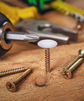 Plastic Self Tapping and Self Adhesive Screw Hole Covers for Wood Furniture, white cap on screw in wooden surface with tools nearby.
