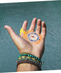 Hand holding Orienteering Compass Ruler And Pointer For Hiking And Camping, Acrylic Survival Navigation Tool by a lake