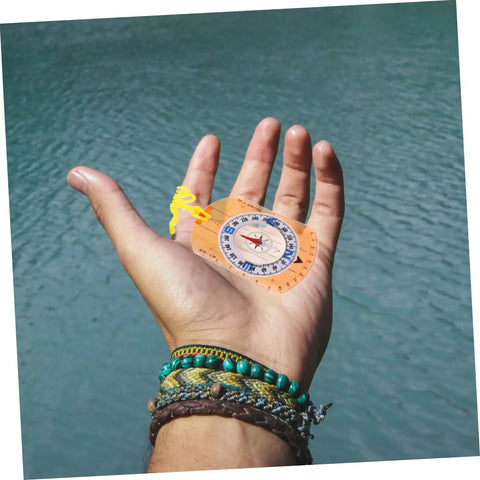 Hand holding Orienteering Compass Ruler And Pointer For Hiking And Camping, Acrylic Survival Navigation Tool by a lake