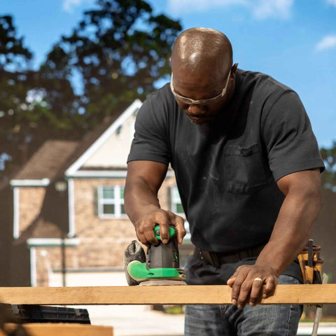 Person using 18V Cordless 5 Inch Random Orbital Sander With Top Notch Dust Collection on wood outside a house