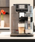 Top Shelf Super Automatic Espresso Machine Crafting One Touch Cappuccino Latte Macchiato Ristretto And Flat White For Your Kitchen Game Changing Setup In Anthracite with glass of latte and milk frother.