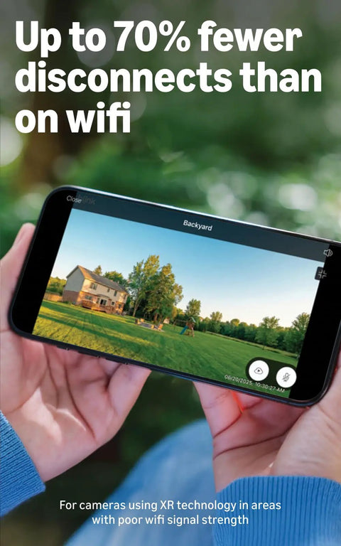 Person holding a smartphone displaying live video feed from Extended Range Wireless Outdoor Security Camera System With Four Cameras 10x Coverage Powered By XR Technology And Sync Module XR Plus Weatherproof Night Vision Simple DIY Setup For Yard And Home Surveillance, showing a backyard with trees.