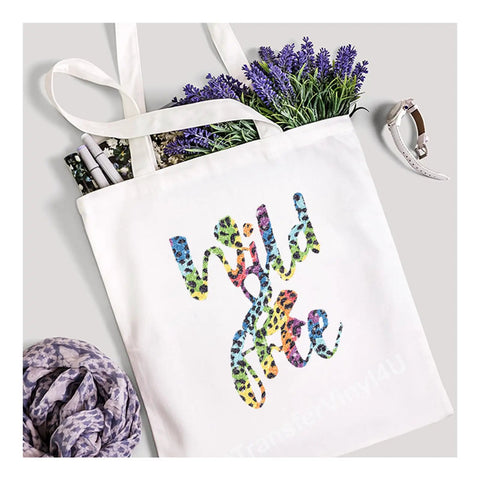 White tote bag with 'Wild & Free' in colorful tiger print vinyl from Glitter Animal Pattern Heat Transfer Vinyl Tiger Print 12x12 Inch Sheet For T Shirts And Fabrics Iron On Dope DIY Craft Supplies With Bold Colors And Rough Glitter Texture For Custom Tees.