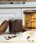Two 17 Oz glass jars with tight wood lids, one with coffee beans and one with pasta, from 24 Pack Glass Canister Set With Tight Wood Lids For A No Sweat Pantry Setup.