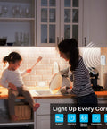 Mother and child cooking with Motion Sensor Under Cabinet Lights Plug In LED Strip Lights Indoor illuminating the kitchen. UL FCC adapter visible.