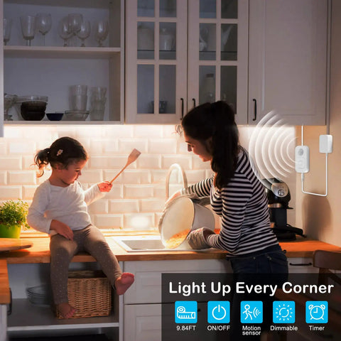 Mother and child cooking with Motion Sensor Under Cabinet Lights Plug In LED Strip Lights Indoor illuminating the kitchen. UL FCC adapter visible.