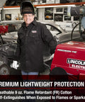 Man wearing Black 9 Oz Flame Resistant Cotton Welding Shirt With Custom Fit, Medium, working in a metal workshop with machinery.