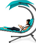 Woman reading on an outdoor hanging curved steel chaise lounge chair swing with built-in pillow and removable UV resistant canopy teal.