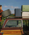 Four 20-inch hard-shell carry-on luggage suitcases with wheels on a car roof rack; black, blue, green, and white.