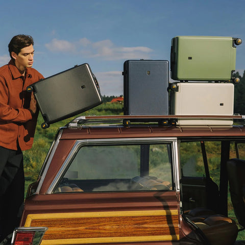 Four 20-inch hard-shell carry-on luggage suitcases with wheels on a car roof rack; black, blue, green, and white.