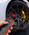 No Fuss Tpms Reset Tool For Universal Vehicle Tire Pressure Sensor Activation And OBD2 Programming in hand near tire.