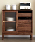 Vintage wooden cabinet with sliding door, glass panel, and three drawers, decorated with kitchenware and toaster on top.
