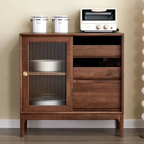 Vintage wooden cabinet with sliding door, glass panel, and three drawers, decorated with kitchenware and toaster on top.