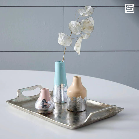 Three decorative ceramic vases in pastel pink, turquoise, and beige with metallic silver leaf bases on a silver tray.
